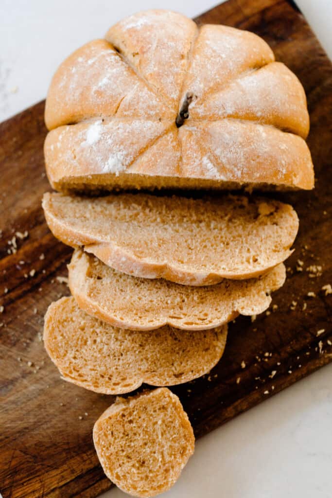 overhead photo of a sliced loaf of pumpkin shaped bread on an antique cutting board