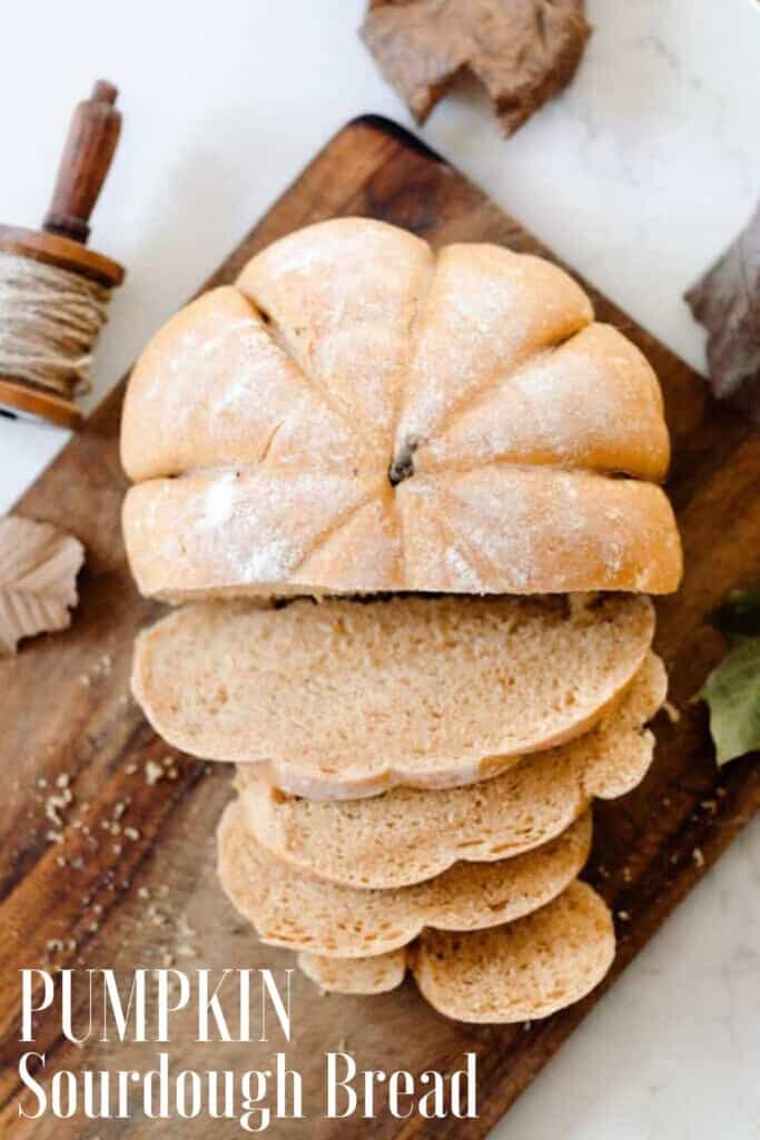 loaf of pumpkin sourdough bread sliced on a old cutting board on a white countertop