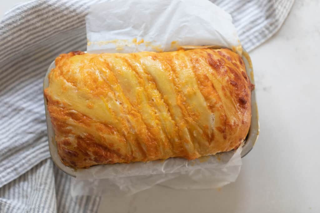 overhead photo of a loaf of cheesy sourdough bread in a loaf pan on a white countertop