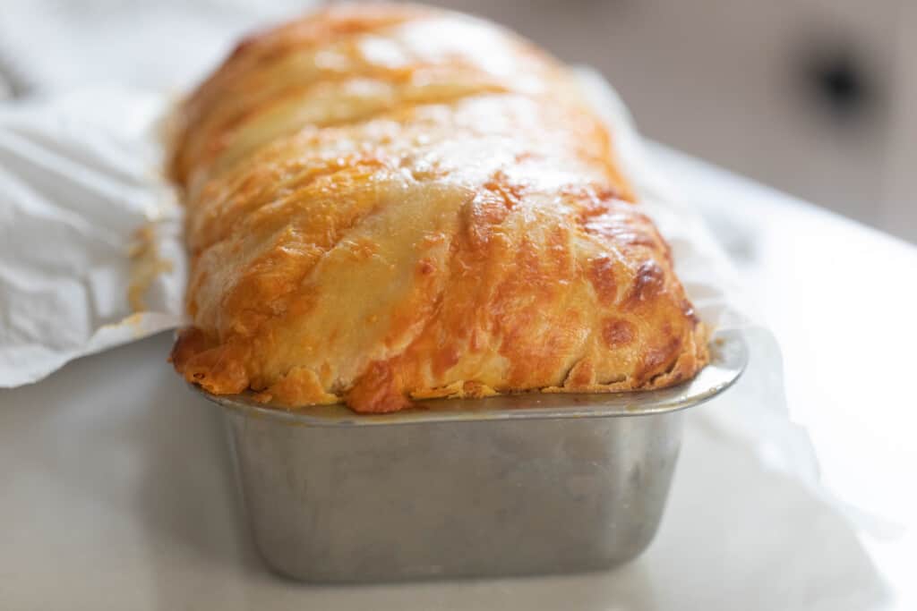 loaf of sourdough cheese bread in a stainless loaf pan on a white countertop