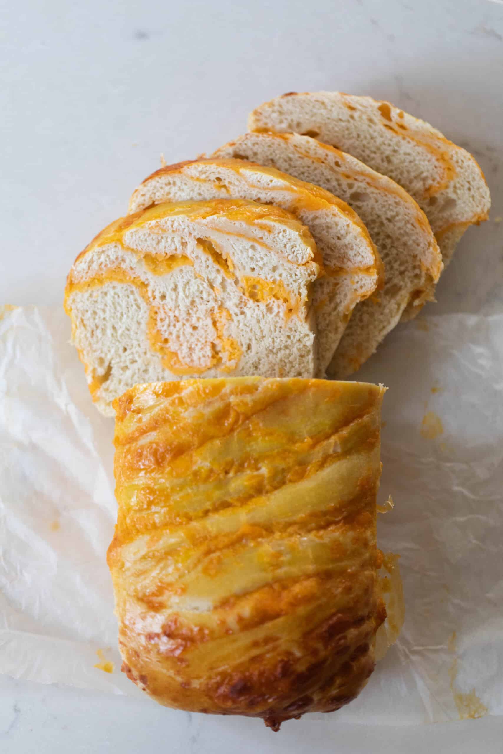 a loaf of sourdough cheese bread with half the loaf sliced into pieces on parchment paper on a white countertop