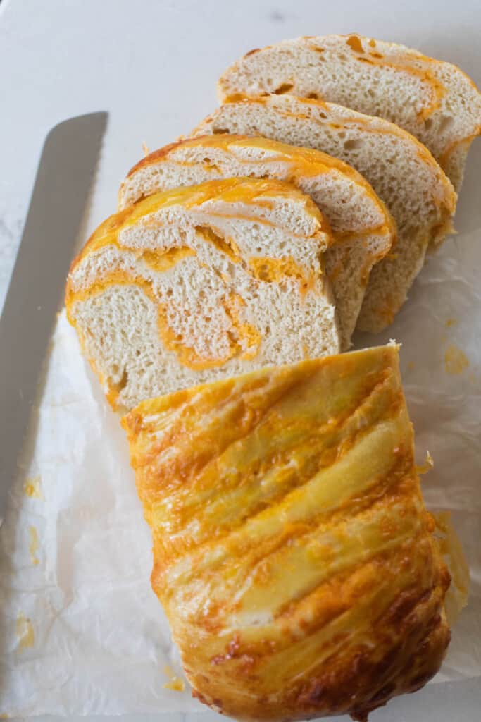 loaf of sourdough cheese bread sliced up on parchment paper with a bread knife to the left