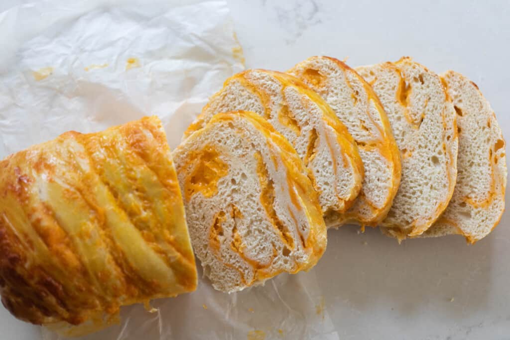 A loaf of cheese sourdough bread cut into four slices on a white countertop