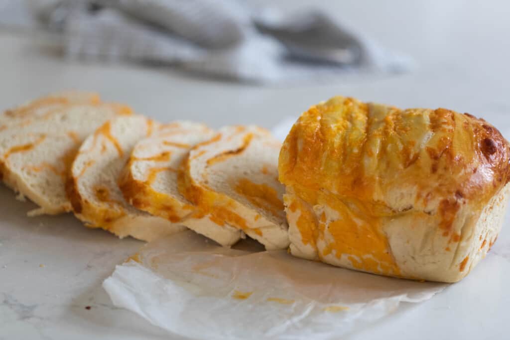 loaf of sourdough cheese bread sliced up on a white quartz countertop