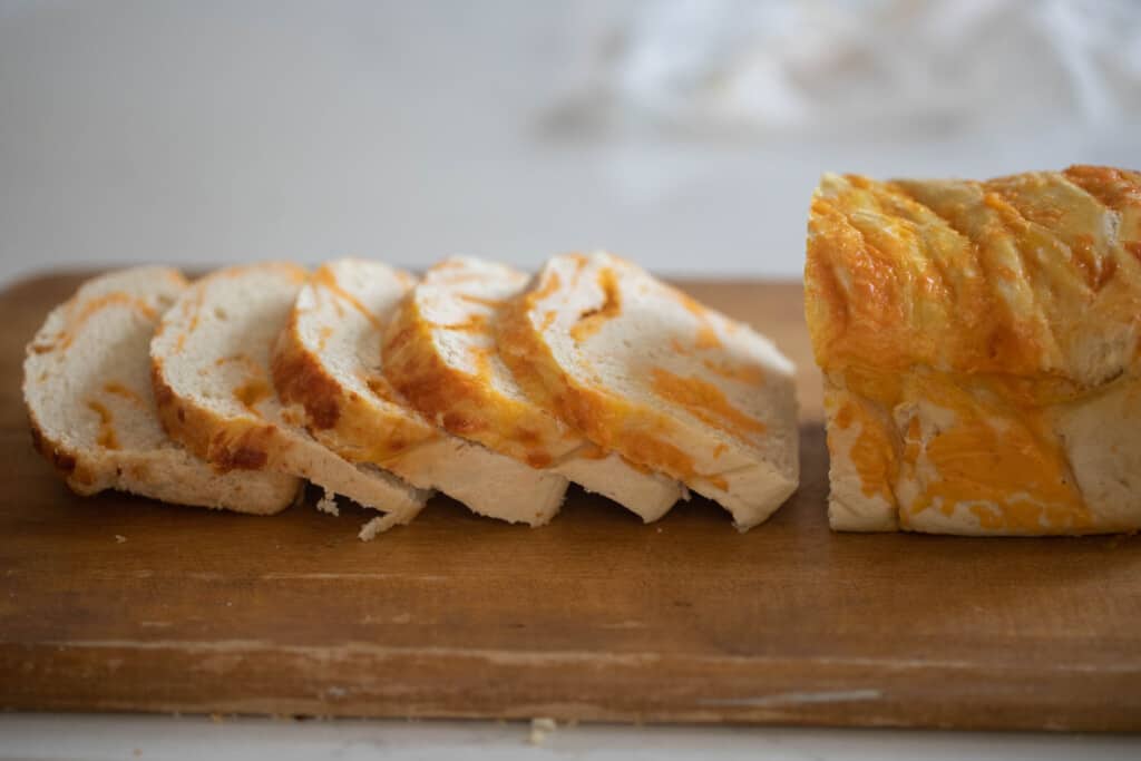 loaf of sourdough bread with swirls of cheese throughout sliced on a wooden cutting board