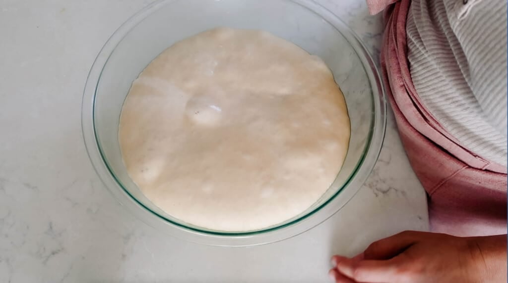 sourdough bread dough in a glass bowl on a white countertop