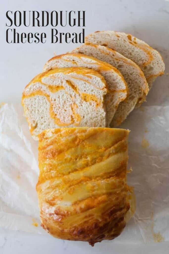 a loaf of sourdough cheese bread with half the loaf sliced into pieces on parchment paper on a white countertop