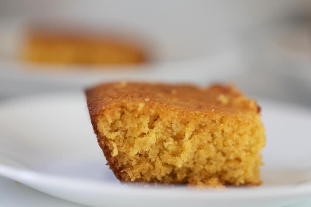 close up of the side view of a square slice of sourdough cornbread on a white plate