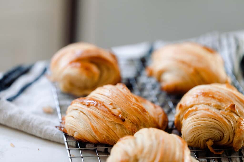 five sourdough croissant rolls on a wire rack that is sitting on a white and black stripped towel