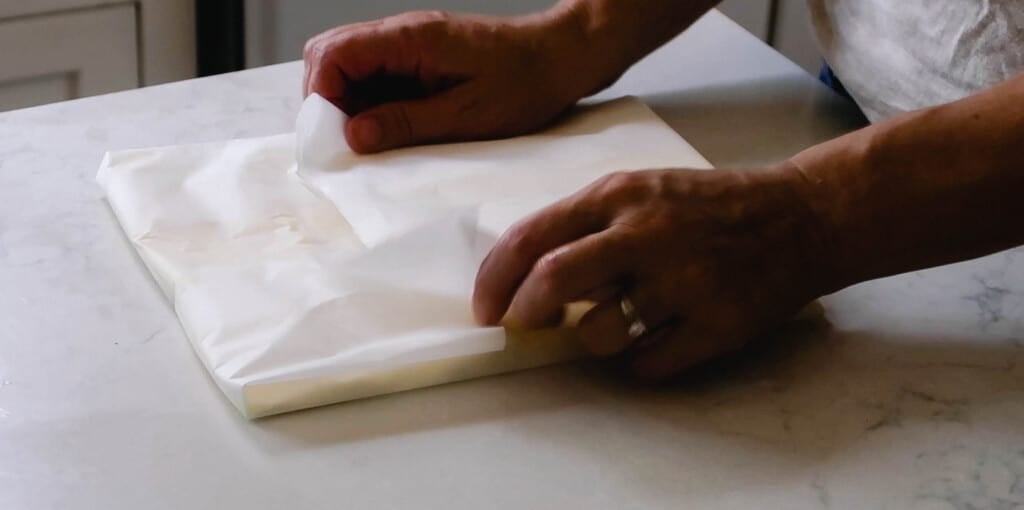 folding parchment paper over butter on a white countertop