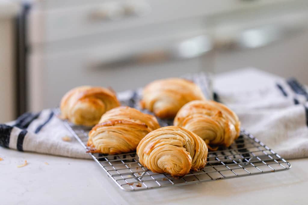 five sourdough crescent rolls on a wire rack that is half on a black and white stripped towel and half on a countertop