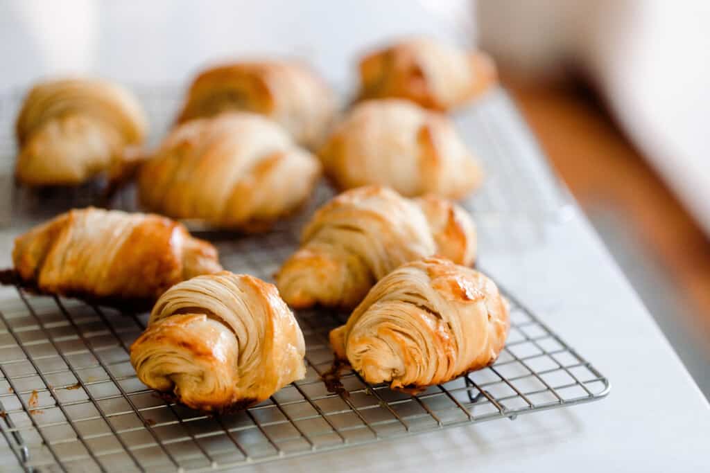 nine sourdough crescent rolls resting on a wire rack on a white countertop