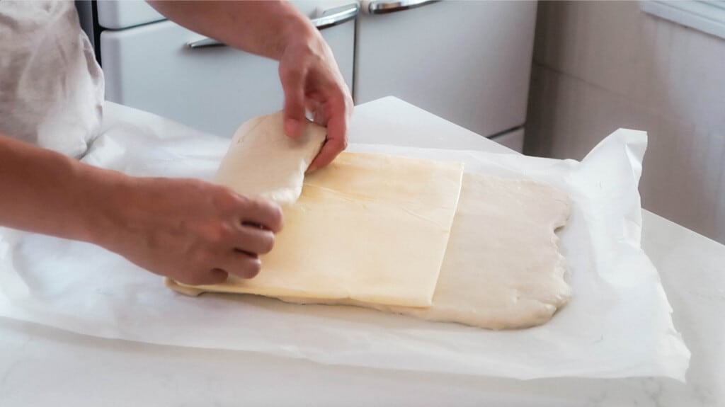 hands folding croissant dough over a butter packet into thirds