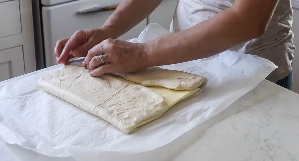 hands pinching dough over butter on parchment paper
