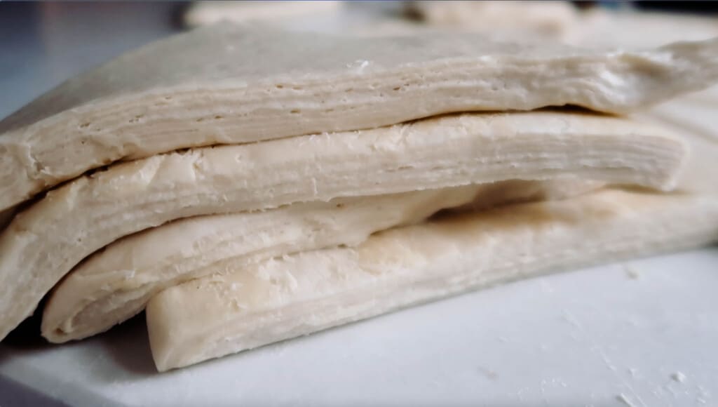 sourdough croissant dough stacked on each other revealing tiny layers of dough and butter