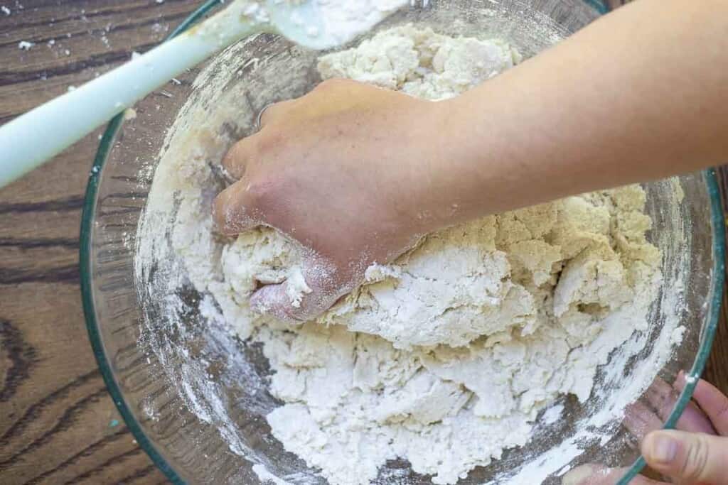 hand mixing gluten free sourdough bread dough in a glass bowl