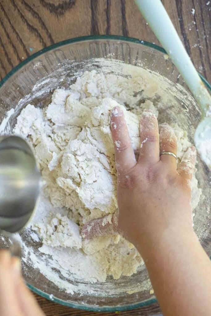 pouring water slowly into a glass bowl of dough