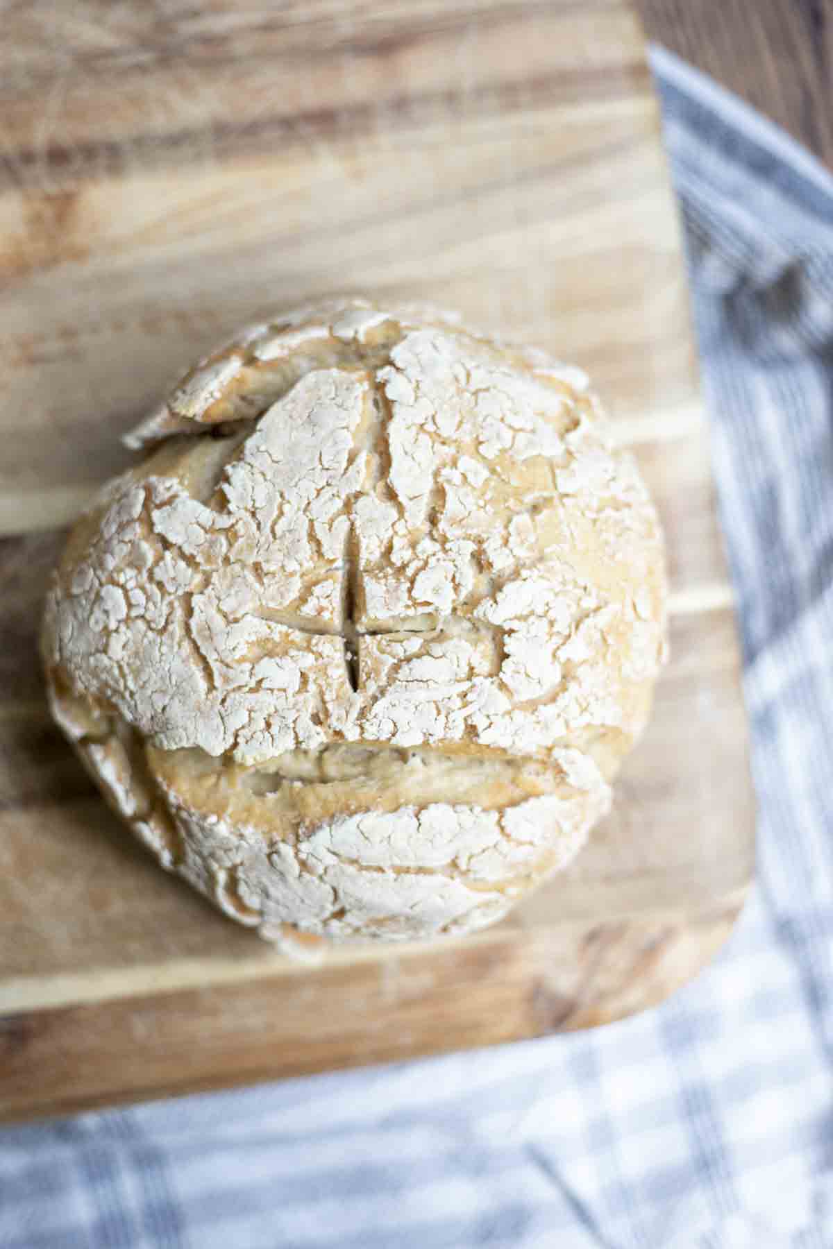 overhead photo of sourdough gluten free bread on a wooden cutting board on top of a white and blue stripped towel