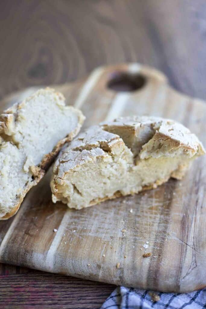 sourdough gluten free bread sliced in half on a wood cutting board on a wood table