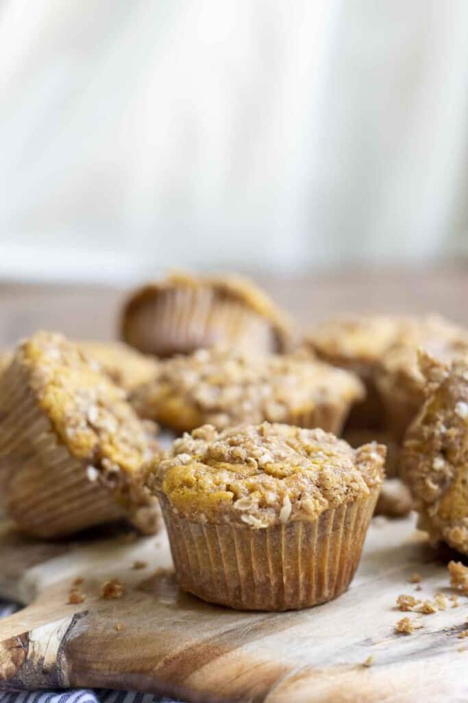 sourdough pumpkin muffins with an oat crumb topping on a wooden cutting board with a white background