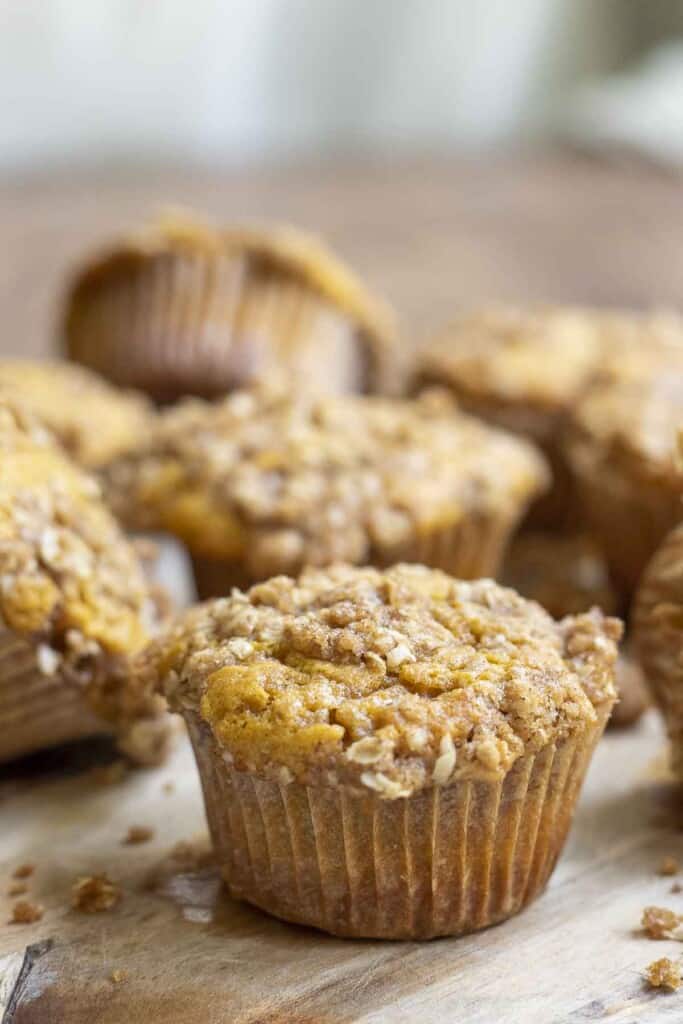 sourdough pumpkin muffin with oat crumb topping spread out on a wood cutting board on a wooden table