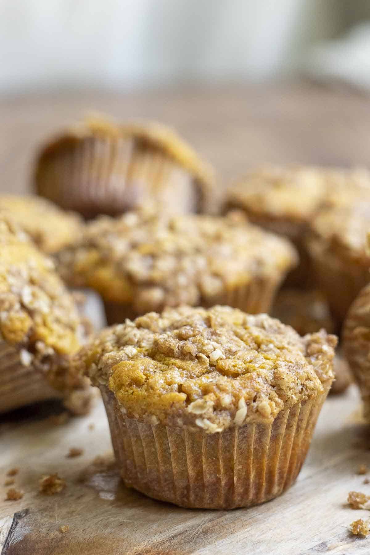 sourdough pumpkin muffin with oat crumb topping spread out on a wood cutting board on a wooden table