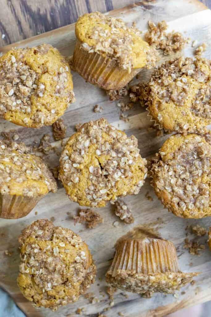 overhead photo of eight sourdough pumpkin muffins with crumb topping on a wood cutting board. Crumble is spread out around the muffins