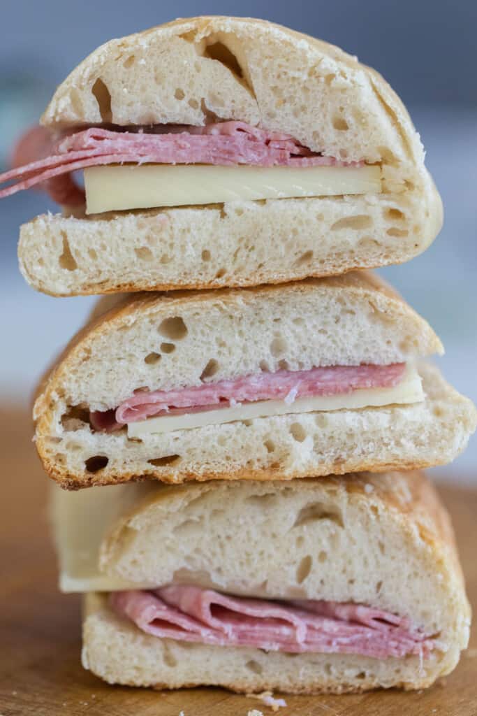 three salami and cheese sandwiches on sourdough sandwich rolls cut in half and stacked on each other 