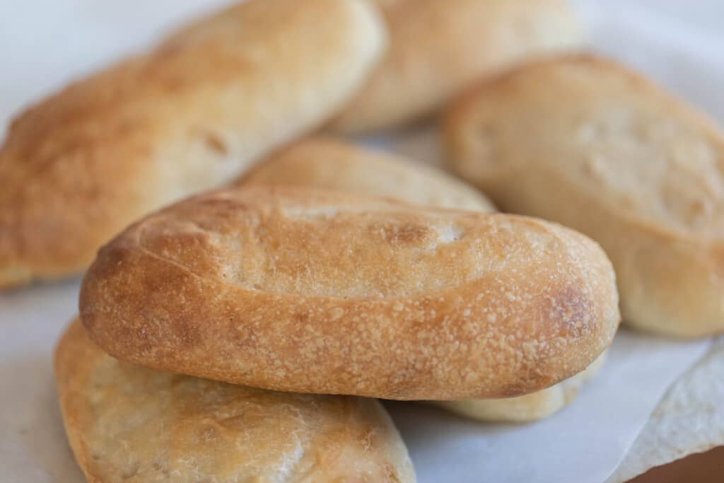 six sourdough sandwich rolls on a white quartz countertop