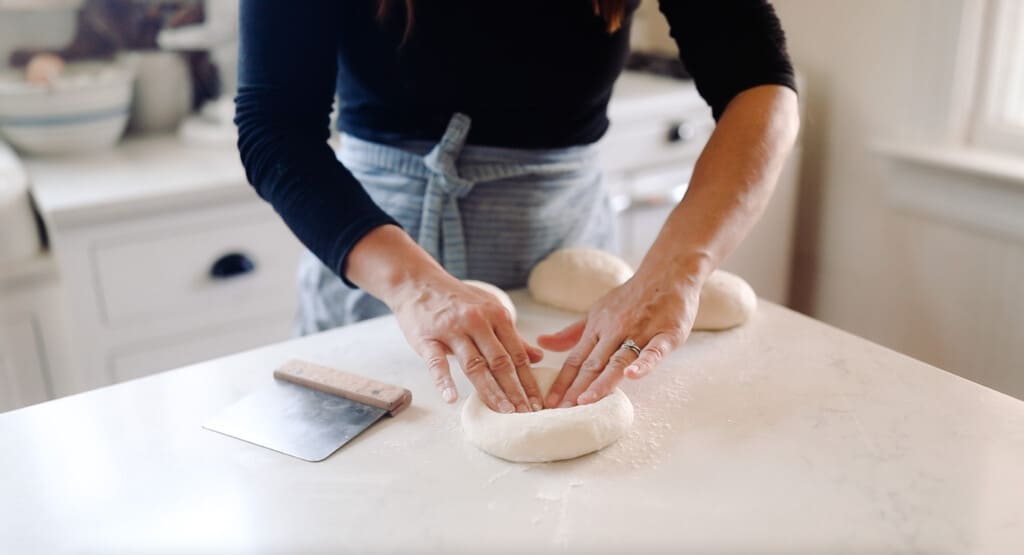 women pressing hands into dough on a white countertop 