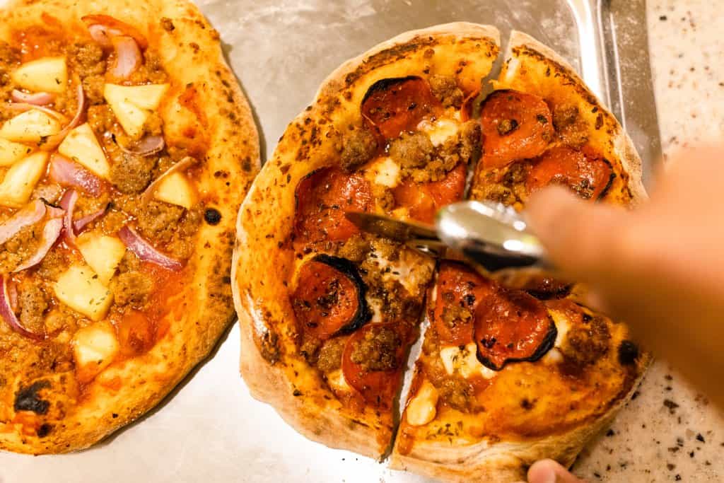 hand using a pizza cutter to slice two pizzas