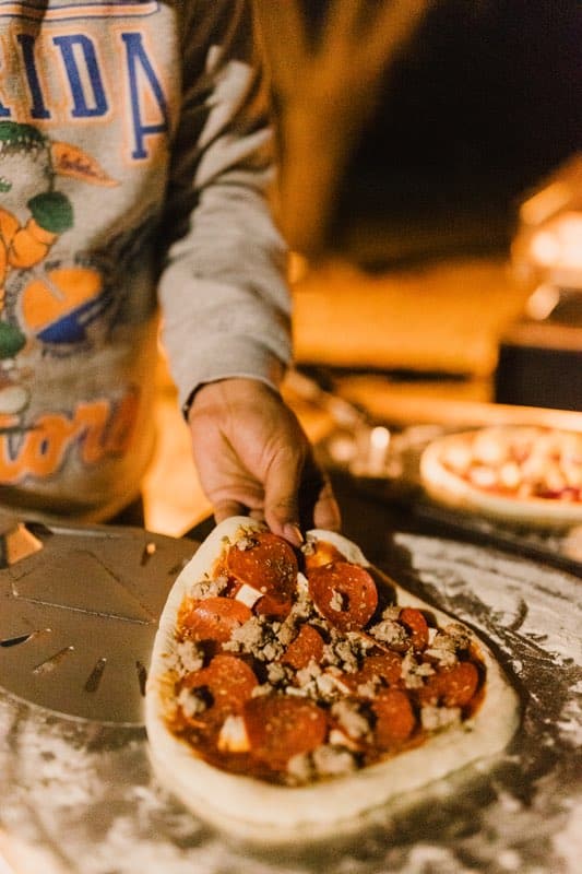 hand placing a pepperoni and sausage pizza onto a metal peel outside on a dark night