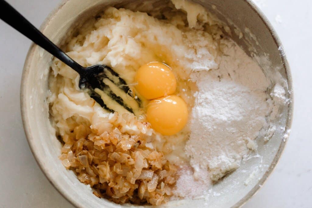 sautéed onions, eggs, flour, mashed potatoes in a large bowl.