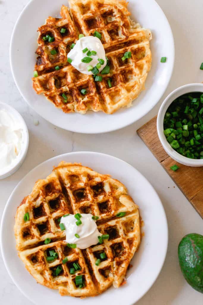 overhead picture of two plates with potato waffles topped with sour cream and chives on a white countertop 