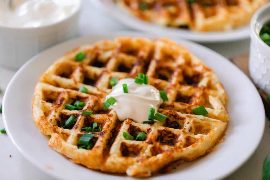 mashed potato waffle topped with sour cream and chives on a white plate