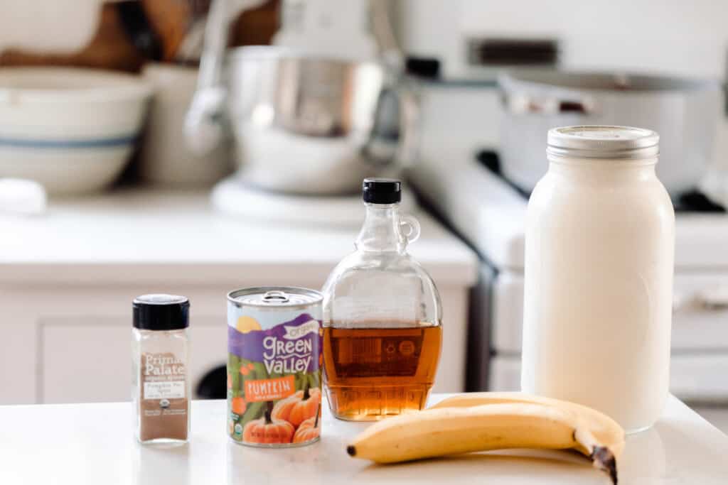 maple syrup, milk, pumpkin puree, banana, and pumpkin spice on a white quartz countertop