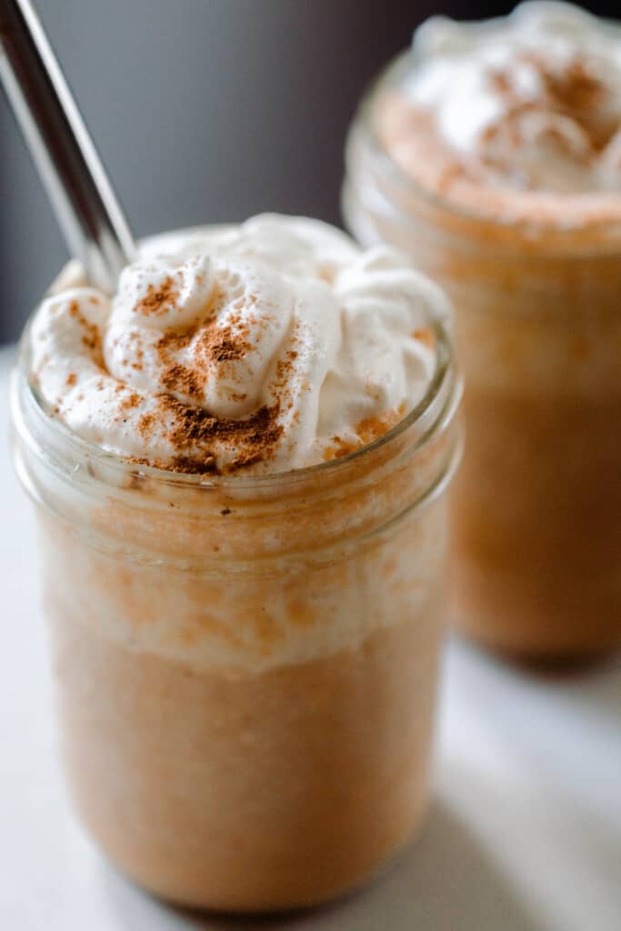 two pumpkin smoothies topped with whipped cream and pumpkin spice in glass mason jars