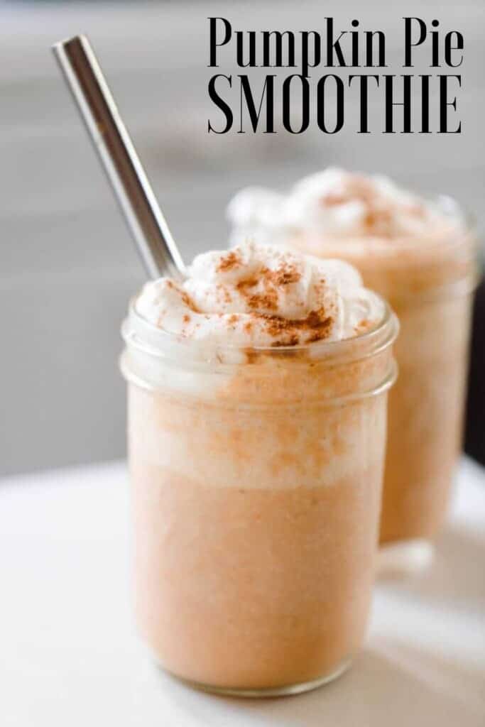 two pumpkin smoothies topped with whipped cream sprinkled with pumpkin spice. A metal straw is in the smoothie and the smoothies sit on a white countertop