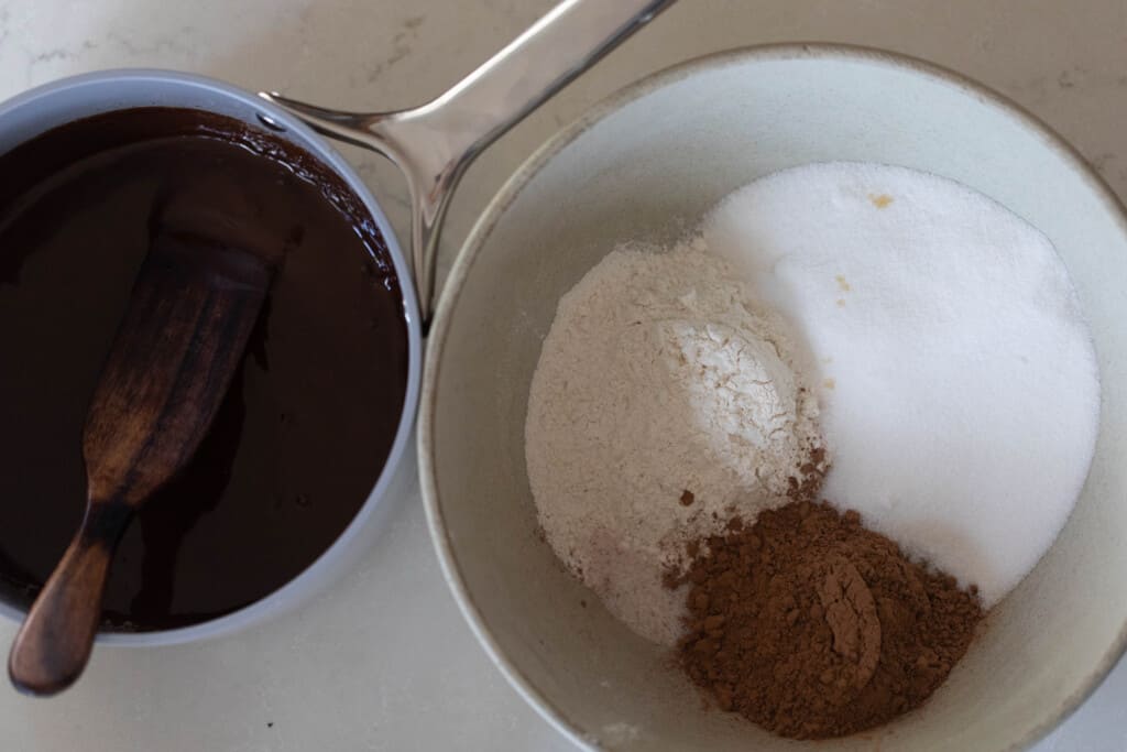 cocoa powder, sugar, and flour in a bowl. A pot of melted chocolate is to the left
