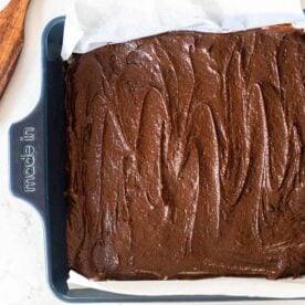 overhead photo of sourdough brownie batter poured into a blue 9x0 baking dish with a wooden spatula in the back right corner.