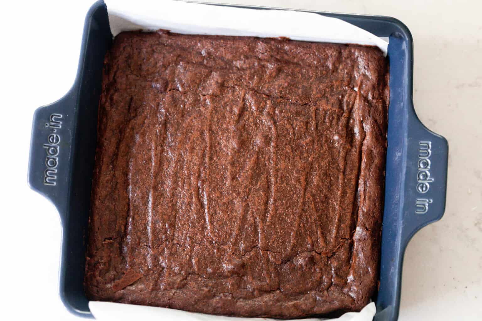 Sourdough brownies fresh out of the oven in a parchment lined blue baking dish.
