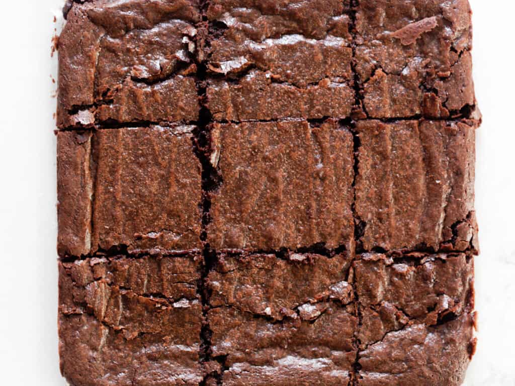close up of a slab of brownies cut into 9 equal pieces on white parchment paper.