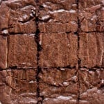 close up of a slab of brownies cut into 9 equal pieces on white parchment paper.