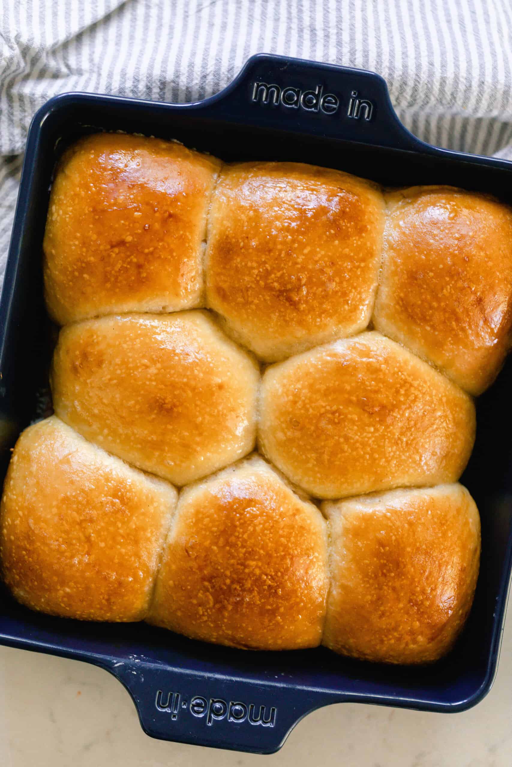 overhead photo of sourdough dinner rolls with a deep golden shiny top in a dark navy baking dish