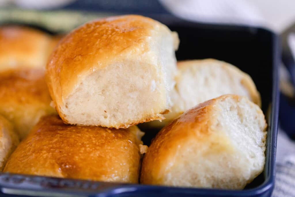 sourdough dinner rolls pulled apart and stacked on each other in a navy baking dish. The soft and fluffy rolls have a deep golden color and a butter top