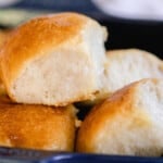 sourdough dinner rolls pulled apart and stacked on each other in a navy baking dish. The soft and fluffy rolls have a deep golden color and a butter top