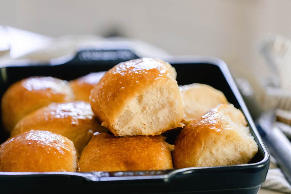 sourdough dinner rolls freshly baked out of the oven with a golden crust and fluffy interior stacked on top of each other in a navy baking dish on a white kitchen island