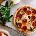 fresh baked sourdough pizza with pepperonis and basil on a quartz countertop with fresh basil and a cutting board to the left