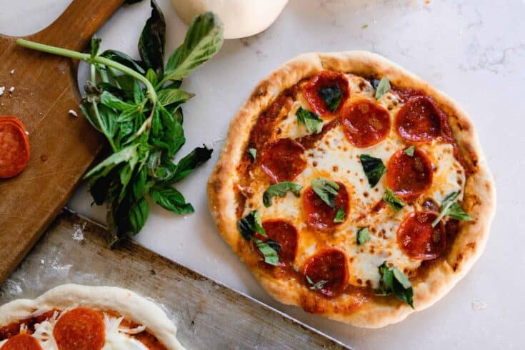 fresh baked sourdough pizza with pepperonis and basil on a quartz countertop with fresh basil and a cutting board to the left