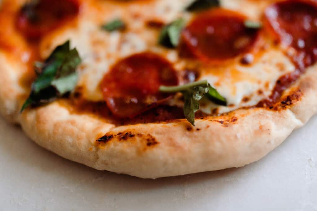 close up picture of sourdough pizza crust on a pepperoni, cheese, and basil pizza.